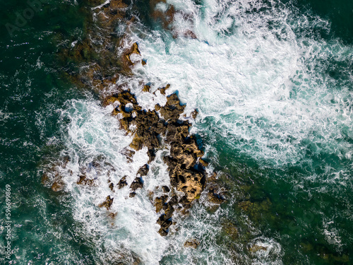 Aerial view of a rough sea crashing against rocks next to a lighthouse (Chania, Crete, Greece)