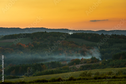 sunset colors over forests and fields, smoke over trees