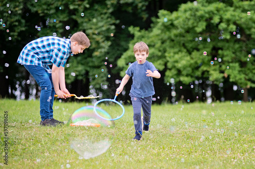 Summer holidays. Schools out. Two brothers playing with soap bubbles in the park. Cheerful happy family having a picnic. Vacations and trips out of town in nature. 