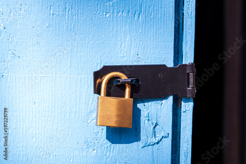brass padlock securing a black metal hasp on a blue wooden door room for text