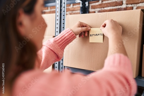 Young beautiful hispanic woman ecommerce business worker putting returned reminder paper on package at office