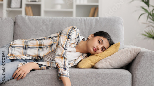 Tired Indian girl slumps on couch feeling listless. Feeling depressed, lack of motivation, sadness, boredom. Exhausted, he collapses on the couch from stress. Burn out.