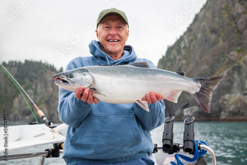 Selective focus view of a happy senior fisherman holding up a nice silver salmon in Alaska