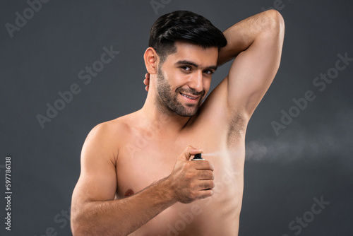 Shirtless handsome Caucasian man using deodorant body spray in light gray isolated background studio shot