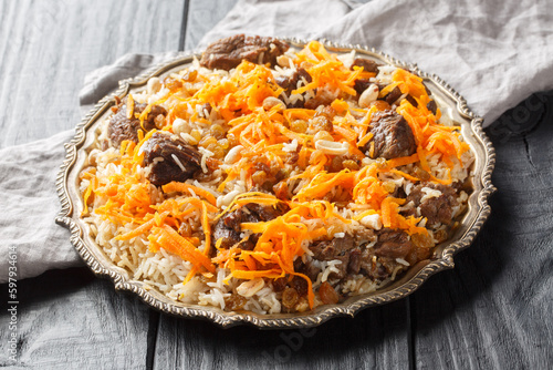 Traditional oriental pilaf with lamb topped with caramelized carrots, raisins and nuts close-up on a platter on a wooden table. horizontal