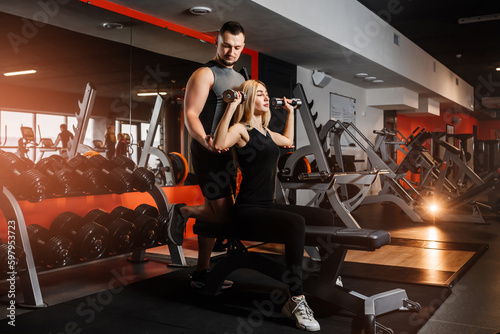 Young couple doing exercises with dumbbells in the gym together.