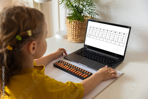 A girl from the back is engaged in mental arithmetic on the abacus online on a laptop, chroma key background. The concept of teaching children to count quickly, Russian mathematics.