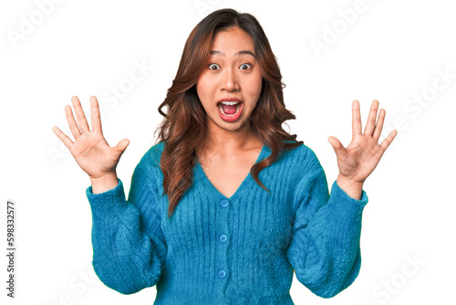 A young chinese woman receiving a pleasant surprise, excited and raising hands.