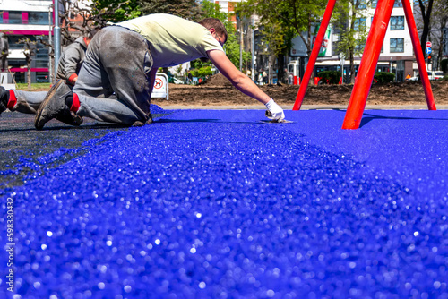 Belgrade, Serbia - April 28, 2023: New childrens playground under construction. A mason hand with trowel spreading and leveling soft rubber crumbs rubber mulch .for children's playground.