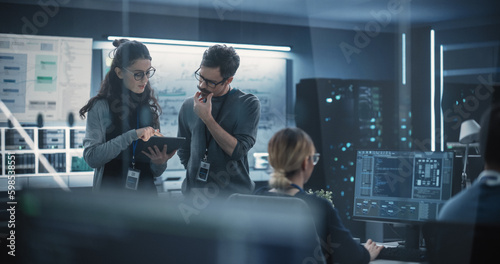 Portrait of Two Creative Young Female and Male Engineers Using Tablet Computer to Analyze and Discuss How to Proceed with the Artificial Intelligence Software. Standing in High Tech Research Office