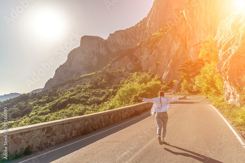 woman running mountain. Happy woman runs along an asphalt road in the middle of a mountainous area. She is dressed in jeans and a white shirt, her hair is braided. A traveler in the mountains rejoices