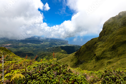 Panoramic view from Mount Pelée hiking track on the tropical island Martinique, France. Lush volcanic mountain vegetation in wide landscape. Saint Pierre village and Caribbean sea in the background.
