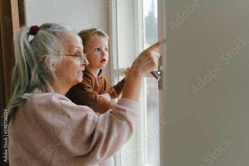 Grandmother with her little grandson looking out of the window.