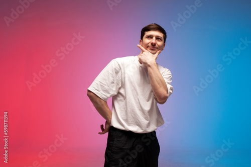 pensive guy in white t-shirt thinks in neon lighting, man dreams and imagines on red blue background