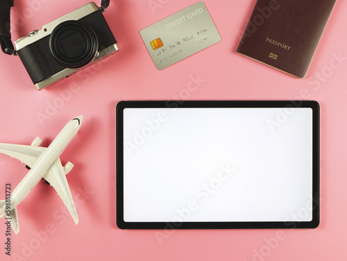 flat lay of digital tablet with blank white screen, airplane model, passport, credit card and digital camera isolated on pink background. travel planning concept.