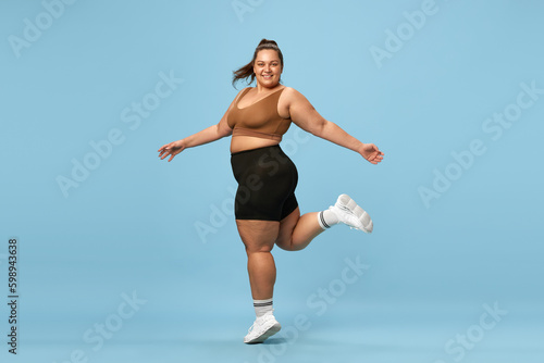 Young, happy, active, overweight woman training in sportswear against blue studio background. Self-love and acceptance. Concept of sport, body-positivity, weight loss, body and health care