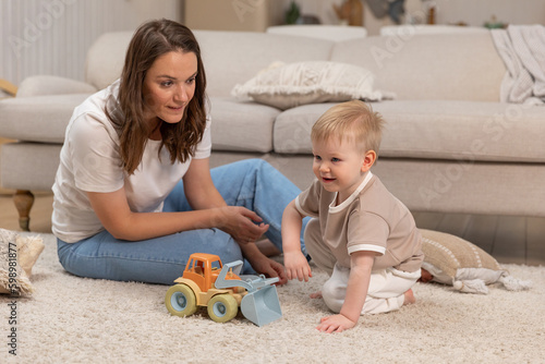 Happy family at home. Mother and baby boy playing with toys at home indoors. Little toddler child and babysitter nanny having fun together. Young woman mom kid son rest in living room