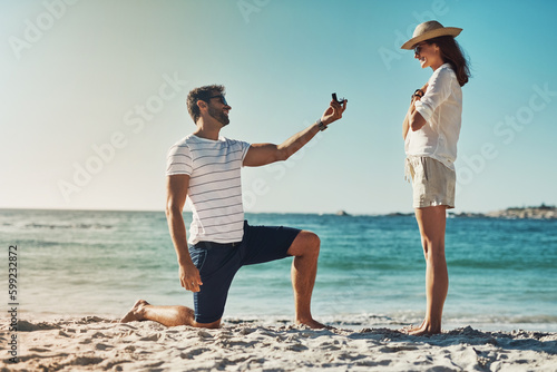 The perfect spot for a summer engagement. Full length shot of a young man proposing to his girlfriend at the beach on a summers day.