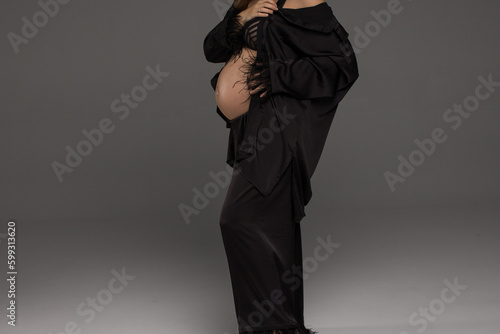 Happy pregnancy woman in black dress on a grey background. Beautiful pregnancy. Person in a black suit.