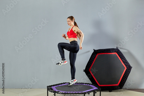 A young athletic girl does a rebound exercise. Fitness trainer in sportswear jumps on a sports trampoline gym.