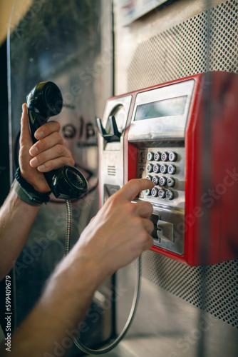 Person dialing a phone number on a public telephone at a payphone booth. Old school telecommunications technology. 