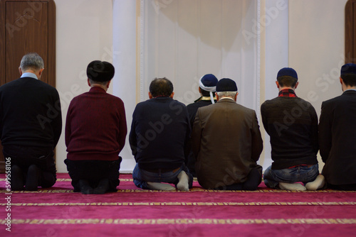 Group of Muslim men and mullah kneeling and praying in a mosque