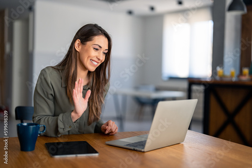 Kind smiling businesswoman, satisfied female entrepreneur waving hand looking at laptop during virtual video conference call in home office.