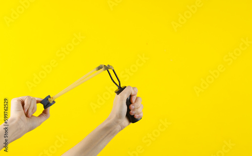 Hand holding a slingshot on a yellow background
