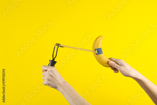 Hands holding slingshot with banana on a yellow background