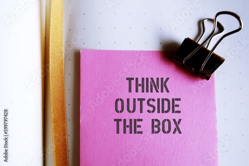 Pink note on notebook with text written THINK OUTSIDE THE BOX , concept of breaking status quo to find innovative solution or create something differently, stand out from the crowd.