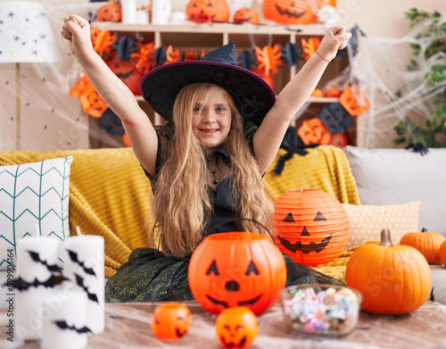 Adorable blonde girl wearing witch costume with winner expression at home