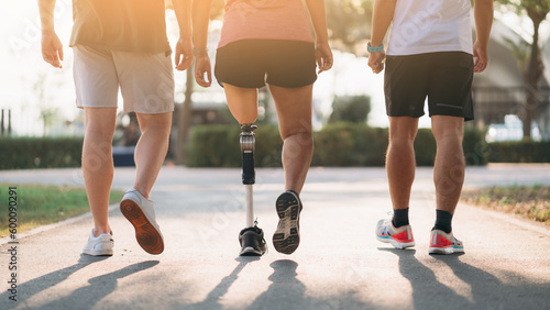 Woman exercising in a park with a friend providing support while using a prosthetic leg. People jogging side by side outside in a park. Female walking and exercise works out outside.