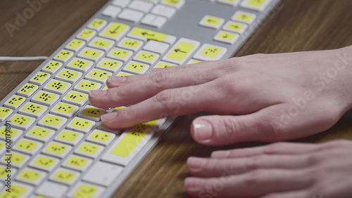 Close-up of a computer keyboard with braille. A blind girl is typing words on the buttons with her hands. Technological device for visually impaired people