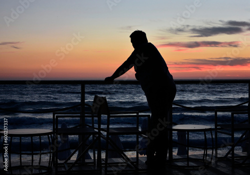 mężczyzna o zachodzie słońca nad morzem, man at sunset by the sea, pensive man leaning against a railing overlooking the seascape and sunset 
