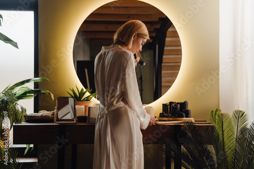 Back view of woman talking on mobile phone while standing in front of mirror in bathroom