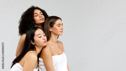 Diversity and youth beauty. Three mixed ladies posing together and looking aside at free space on grey background