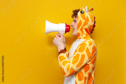 young joyful guy in funny children's giraffe pajamas speaks into megaphone and points his hand to the side