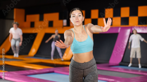 Positive young woman in sport clothes standing expressing different poses in trampoline arena