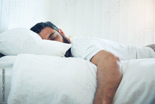 Tired, relax and a man on a bed for sleep, depression and fatigue at home. Rest, napping and a guy sleeping in the bedroom with insomnia, narcolepsy or depressed while lying looking exhausted