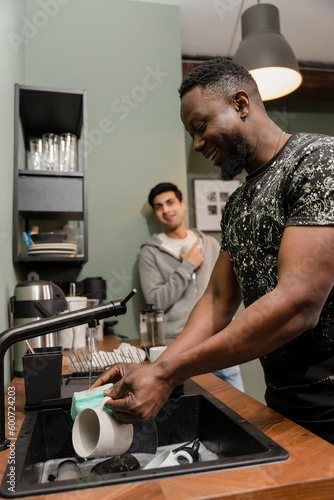 Male flat mates washing dishes in kitchen