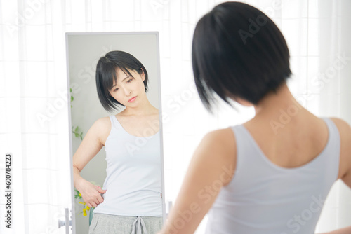 鏡の前でお腹の贅肉を気にする女性