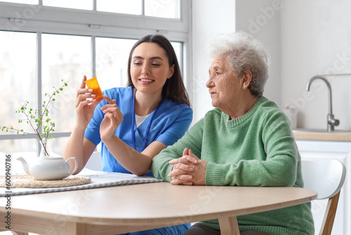 Young caregiver and senior woman taking pills in kitchen