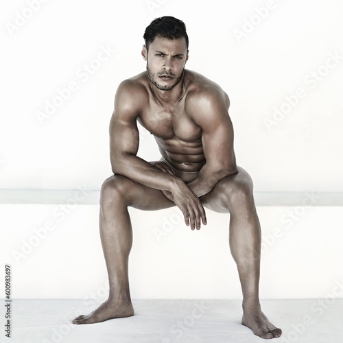 Nude, body and man in portrait isolated on a wall background for health, fitness and wellness. Naked, strong and face of a sexy male model sitting with muscles for power, sports and exercise results