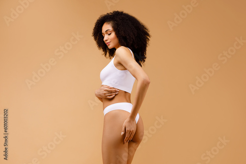 Fitness and strength. Strong and toned black woman proudly showing her well-sculpted body, posing on beige background