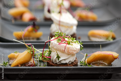 Appetizer dish from savory cream and goat cheese on pumpernickel bread with rhubarb pieces and sprout garnish served on black plates, selected focus