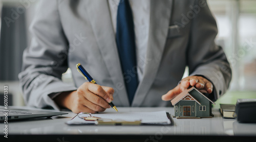 Businessman or real estate agent with house model laying down contract, having contract in place to protect it, signing little agreement form in office, keeping real estate, moving house or renting pr