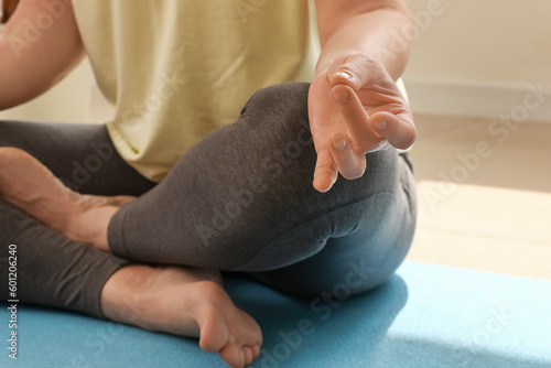 Mature woman meditating while practicing yoga at home, closeup