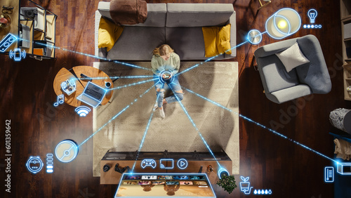 Top View Of Caucasian Woman In the Loft Apartment Sitting On Carpet Next To Couch and Connecting Smartphone to Smart Home System. VFX Edit Visualizing Connected Devices. Laptop, TV, Speaker.