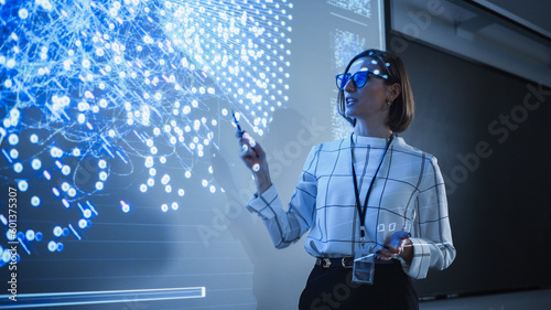 Young University Professor Explaining a Web Development Project to a Group of Students in a Dark Auditorium. Female Teacher Showing a Back-End Programmers Code on a Big Projector Screen