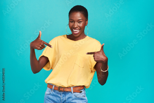 Portrait, crazy and pointing with a black woman in studio on a blue background looking carefree or silly. Smile, fashion and fun with a happy young female hipster feeling confident or playful